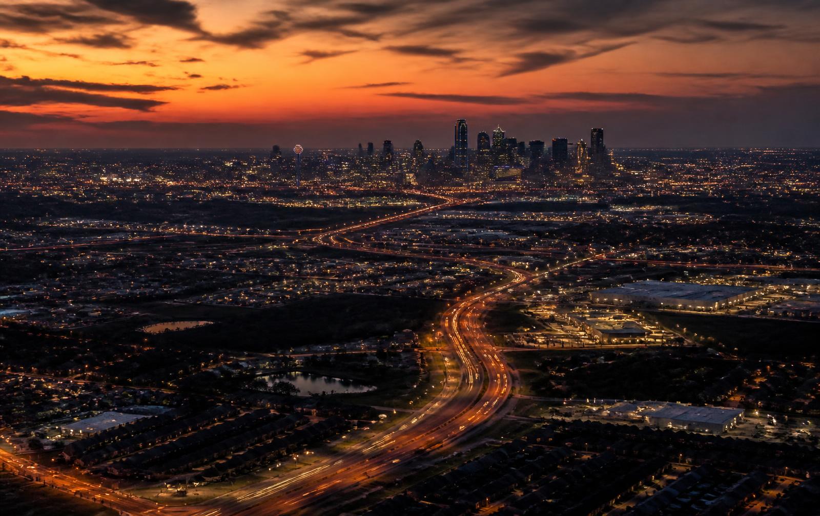 Aerial view of the Dallas–Fort Worth skyline at dusk with surrounding suburban growth corridors